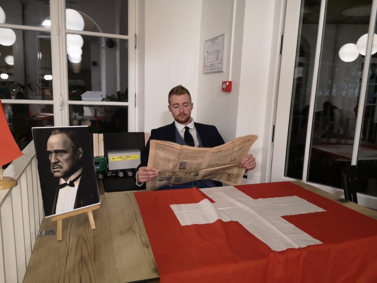 participant-en-costume-lisant-le-journal-devant-le-portrait-du-parrain-lors-du-serious-game-mafia-business