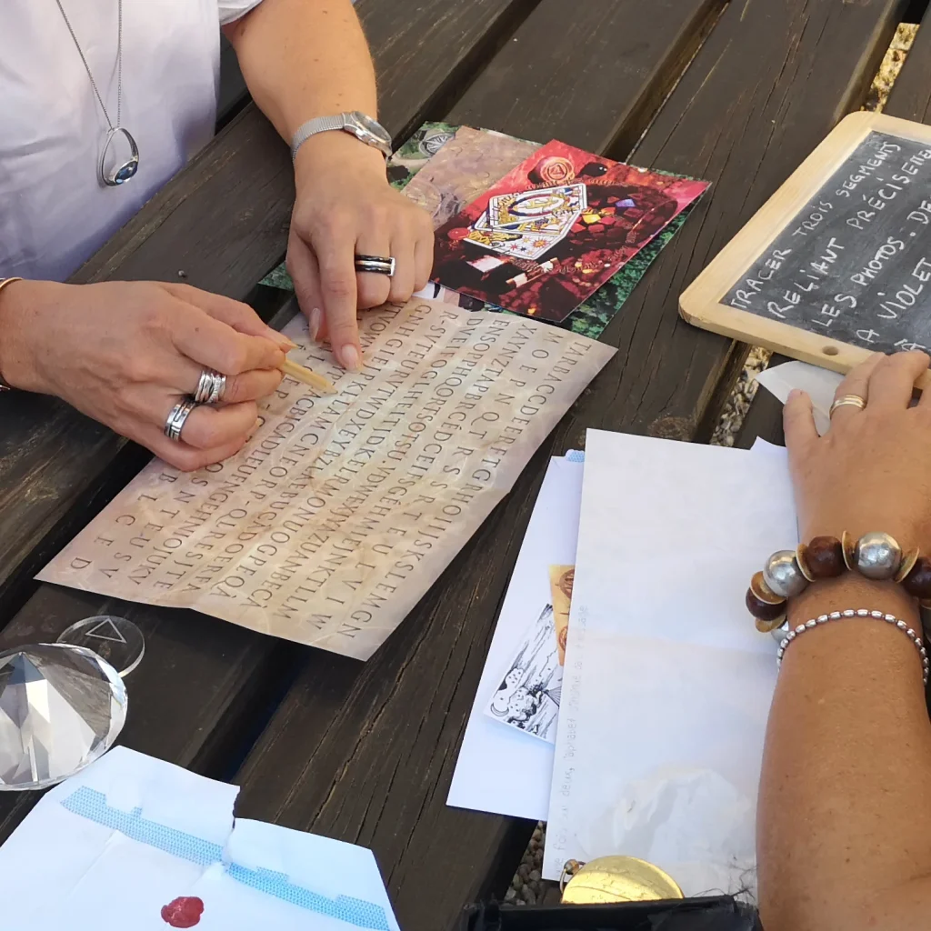 Des mains déchiffrent une grille de lettres sur un parchemin, avec ardoise, photos et cristal, lors d'une chasse au trésor