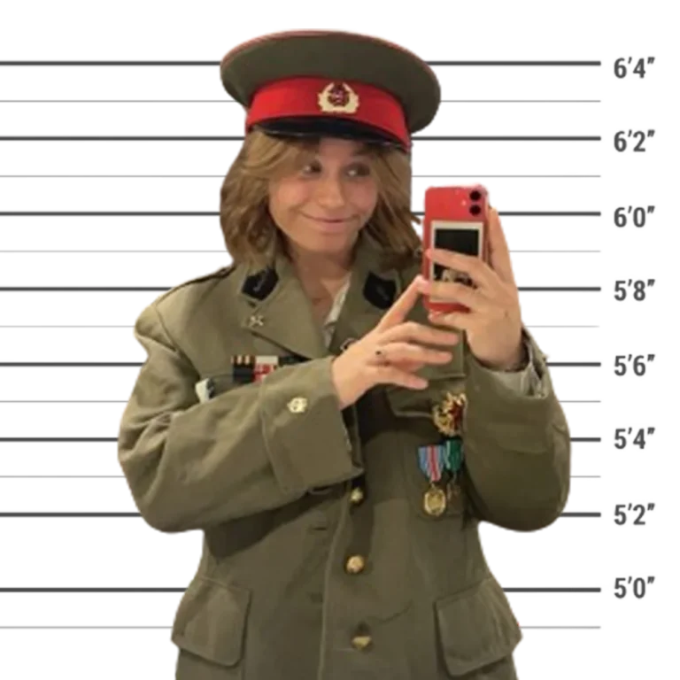 Membre de l'équipe 10Torsions en casquette d'officier et veste militaire à médailles prend un selfie devant une toise