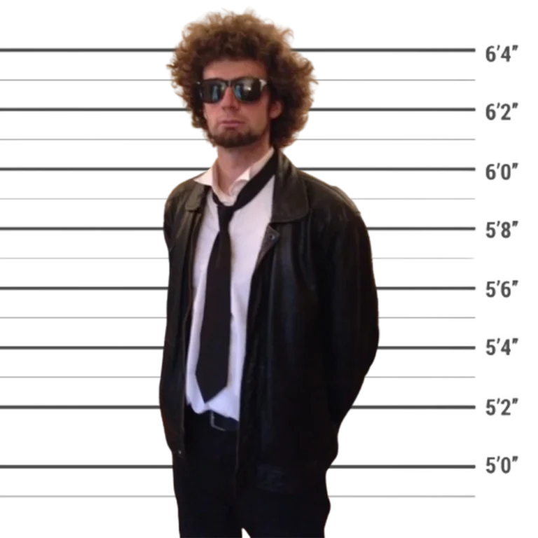 Membre de l'équipe 10Torsions en veste de cuir, cravate desserrée et lunettes noires, coiffure bouclée, devant une toise