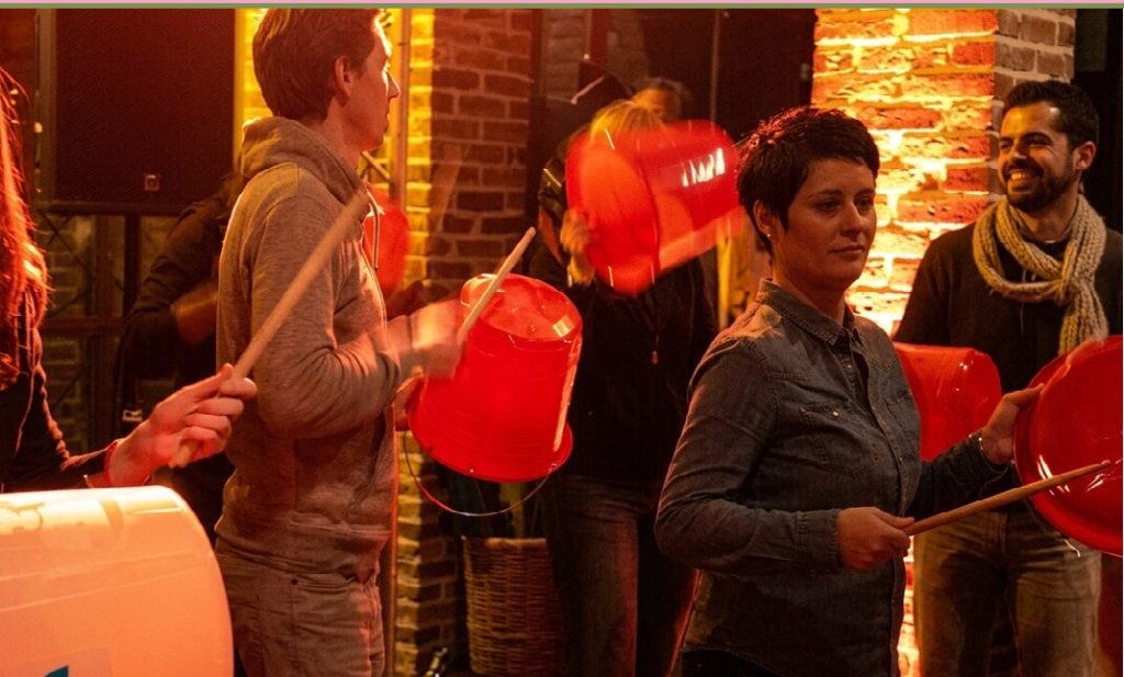 Rythm’n’fun 10Torsions, des participants frappent en rythme sur des bidons rouges, lumière chaude